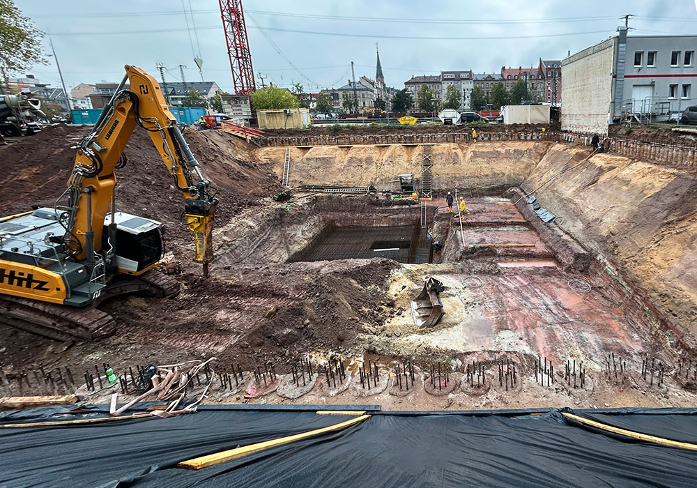 Foto einer Baugrube mit Bagger, Kran und weiteren technischen Strukturen