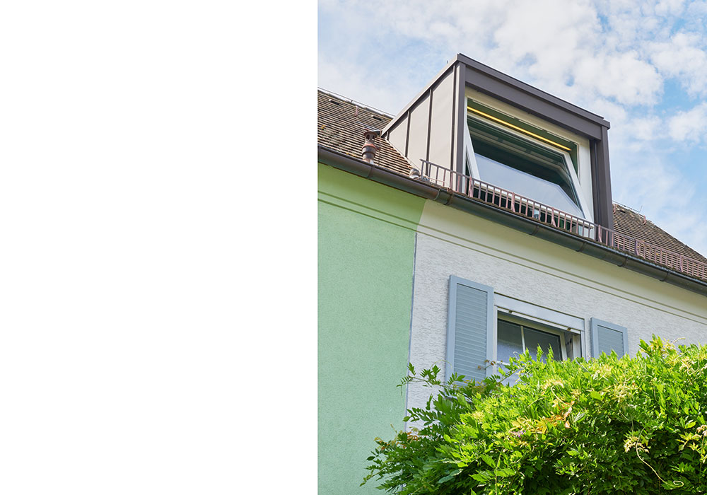 Detailfoto des Daches eines Einfamilienhauses mit Dachgaube, im vordergrund ein angeschnittener Baum.